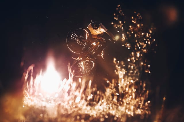 Mountain biker whipping a jump at night, backlit by warm light — Mottolino Bikepark, Livigno