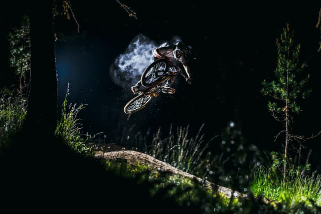 Mountain biker jumping through a dark forest at night — Mottolino Bikepark, Livigno
