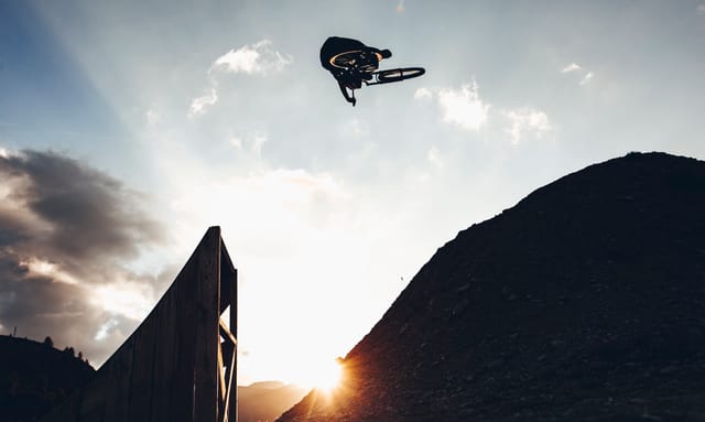 Big whip off a wooden jump, silhouetted at sunset — Mottolino Bikepark, Livigno