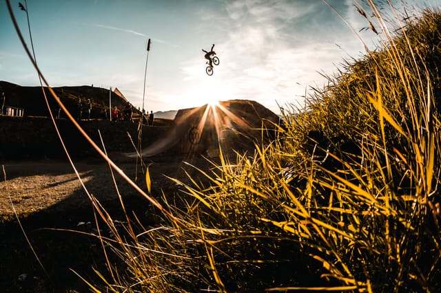 Rider jumping a dirt jump at sunset behind golden grass — Mottolino Bikepark, Livigno