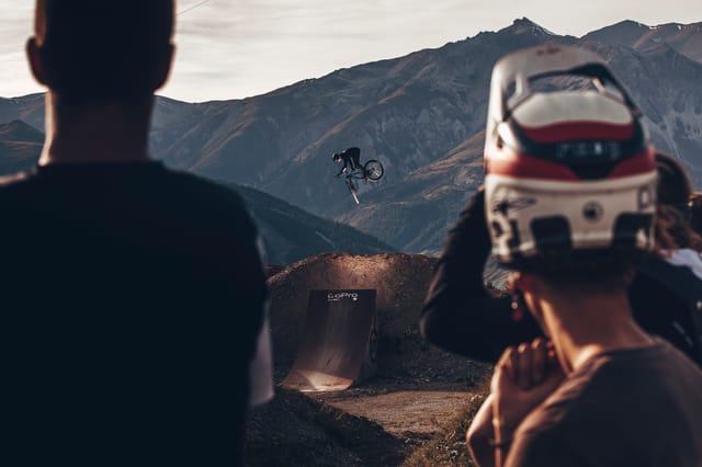 Spectators watching a rider whip a big jump over the mountains — Mottolino Bikepark, Livigno