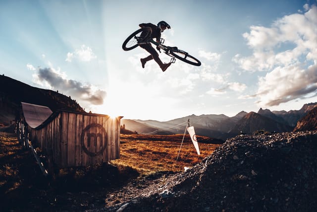 Mountain biker whipping a jump at sunset over the Mottolino mountains, Livigno