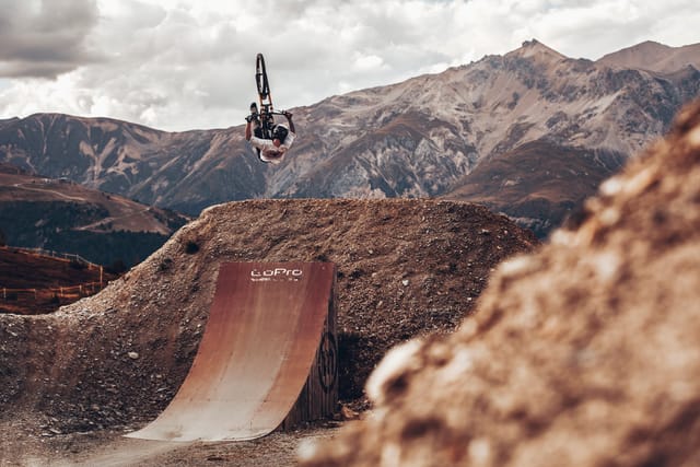 Mountain biker inverting off a ramp with mountains behind — Mottolino Bikepark, Livigno