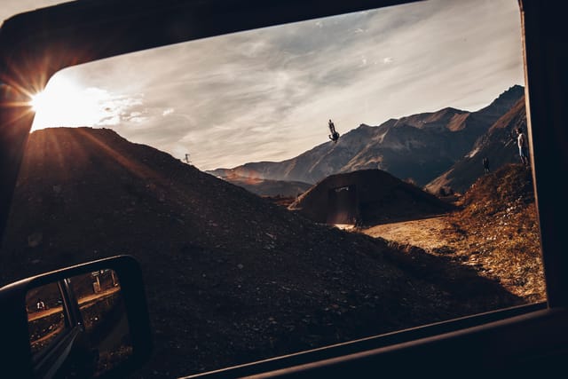 Rider jumping at sunset, framed through a car window — Mottolino Bikepark, Livigno