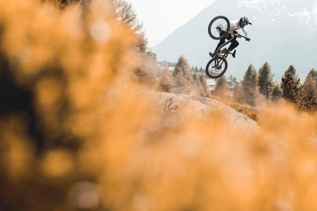 Downhill rider jumping a dirt trail above Livigno in autumn — Mottolino Bikepark